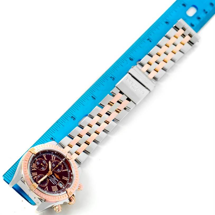 The Breitling Chronomat C13356 Men's Steel and Gold (two tone) Burgundy Dial C13356 Men's Steel and Gold (two tone) Burgundy Dial watch is shown at an angle, displaying the dial, bezel, and full bracelet next to a blue ruler.