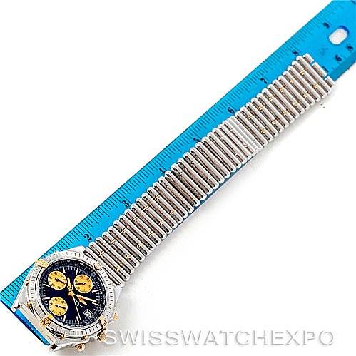 The image shows a Breitling Chronomat B13050 Men's Steel and Gold (two tone) Black Dial B13050 Men's Steel and Gold (two tone) Black Dial watch with a blue dial and a stainless steel bracelet next to a ruler.