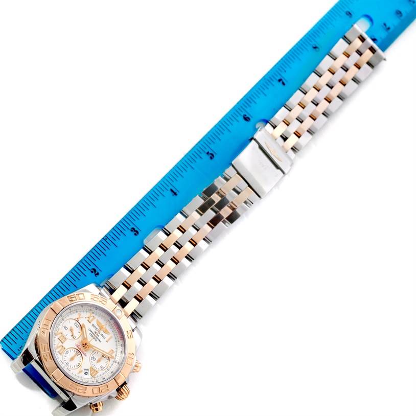 The image shows a Breitling Chronomat CB0140 Men's Steel and Gold (two tone) White Dial CB0140 Men's Steel and Gold (two tone) White Dial watch laid flat beside a blue ruler, highlighting the strap length and dial design.
