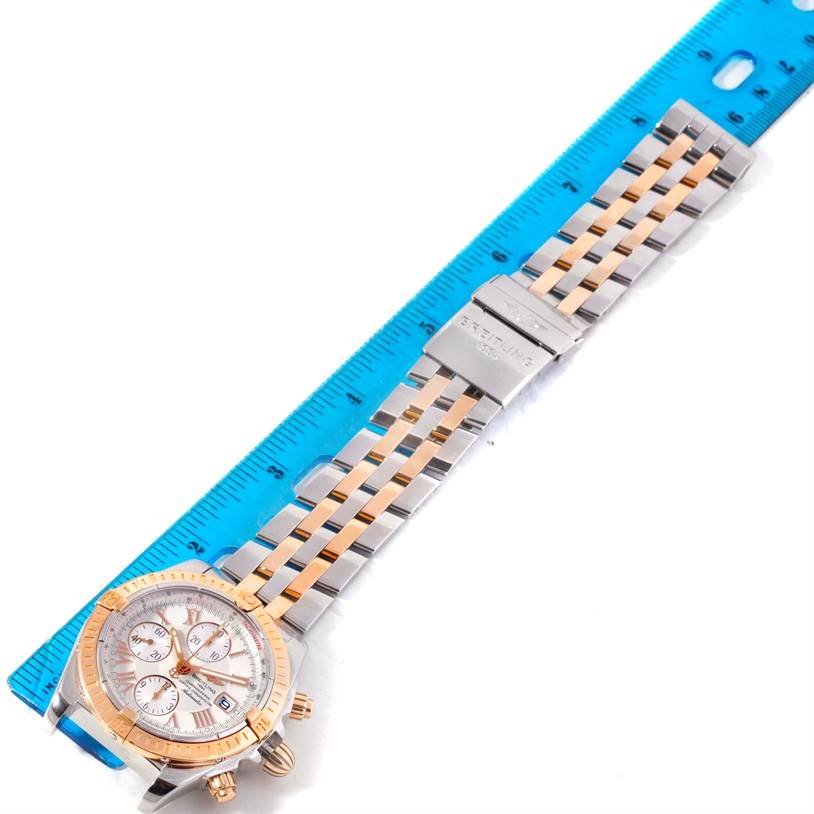The image shows a Breitling Chronomat C13356 Men's Steel and Gold (two tone) White Dial C13356 Men's Steel and Gold (two tone) White Dial watch laid flat against a blue ruler, highlighting its two-tone bracelet and case.