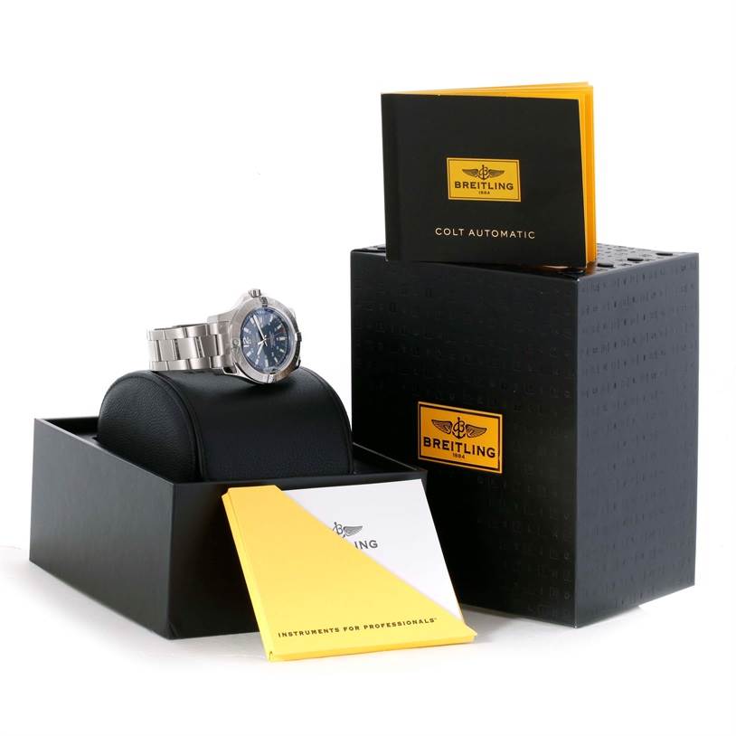 The image shows a Breitling Colt A17388 Men
s Stainless Steel Blue Dial A17388 Men
s Stainless Steel Blue Dial watch at an angle resting on a cushion, along with its box, manual, and warranty card.