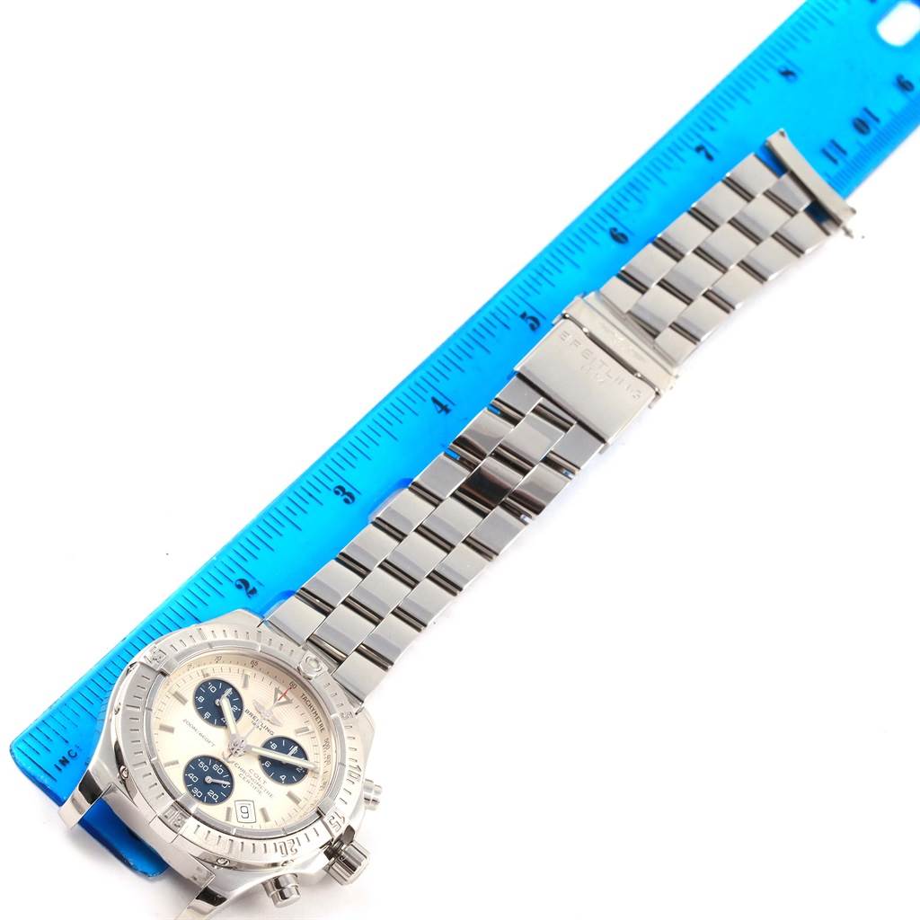 This image shows a Breitling Colt A73380 Men
s Stainless Steel White Dial A73380 Men
s Stainless Steel White Dial watch with its dial and stainless steel bracelet laid next to a blue ruler for scale.