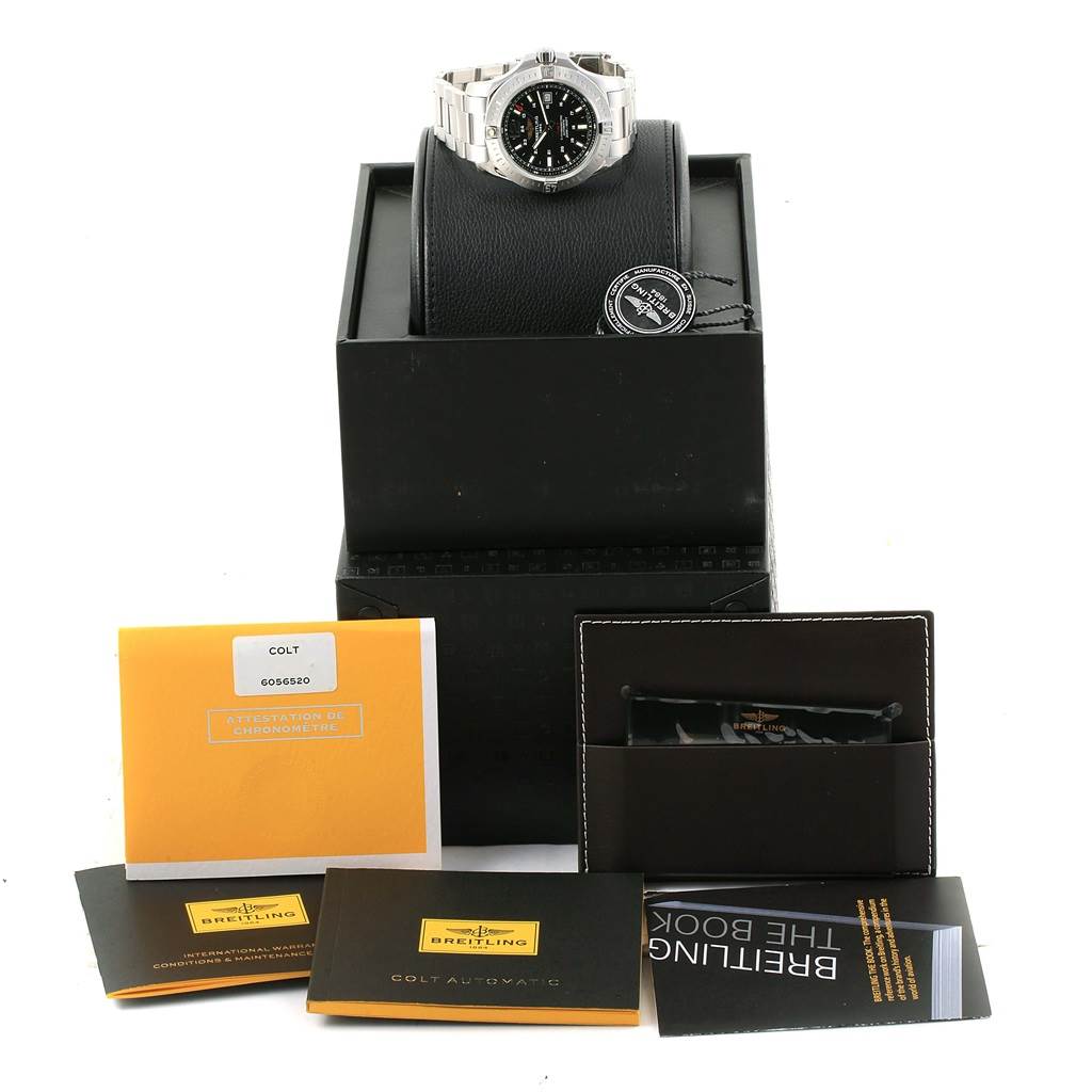 The image shows a Breitling Colt A17388 Men
s Stainless Steel Black Dial A17388 Men
s Stainless Steel Black Dial watch on a stand with its box, manuals, and warranty cards arranged below it.