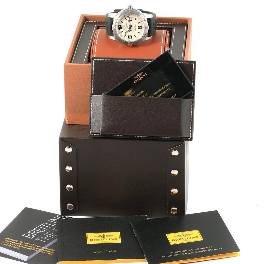 The image shows a Breitling Colt A74387 Men's Stainless Steel Silver Dial A74387 Men's Stainless Steel Silver Dial watch on a stand with its box, warranty card, and manuals arranged around it.