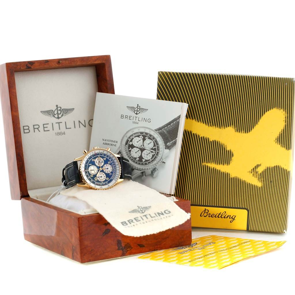 The image shows a Breitling Navitimer K33030 Men
s Yellow Gold Blue Dial K33030 Men
s Yellow Gold Blue Dial watch in its wooden box, with accompanying booklets and a cleaning cloth.