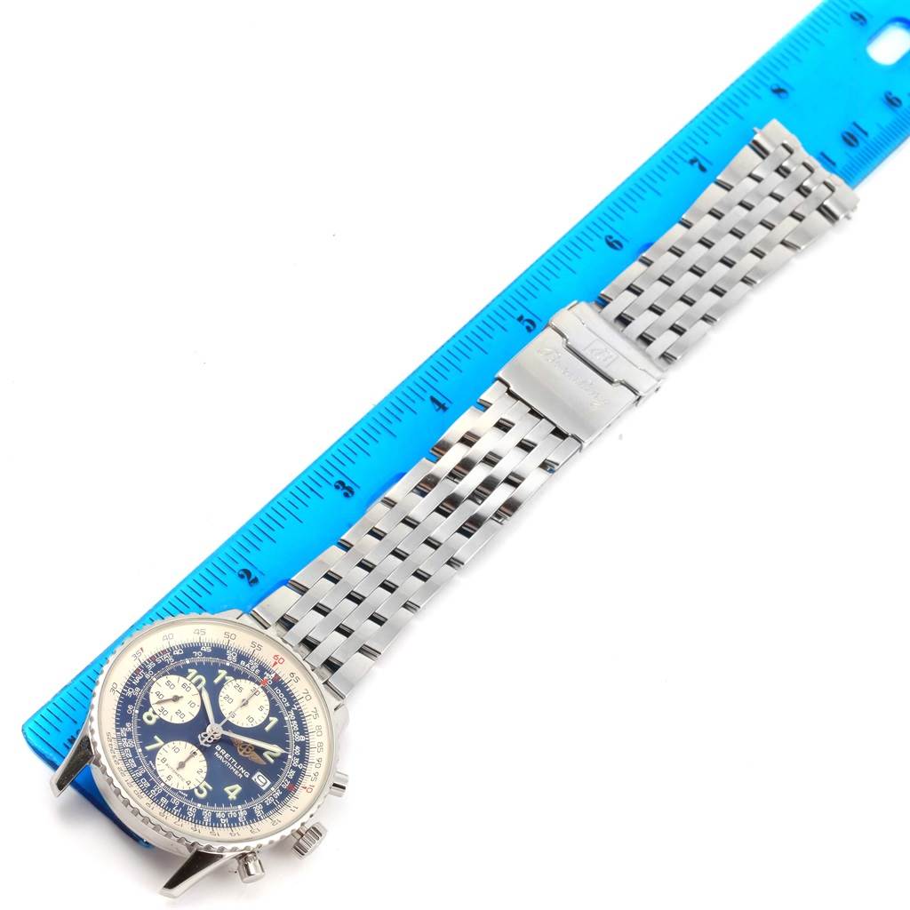The image shows a top view of a Breitling Navitimer A13322 Men's Stainless Steel Blue Dial A13322 Men's Stainless Steel Blue Dial watch with a metal bracelet laid alongside a blue ruler.