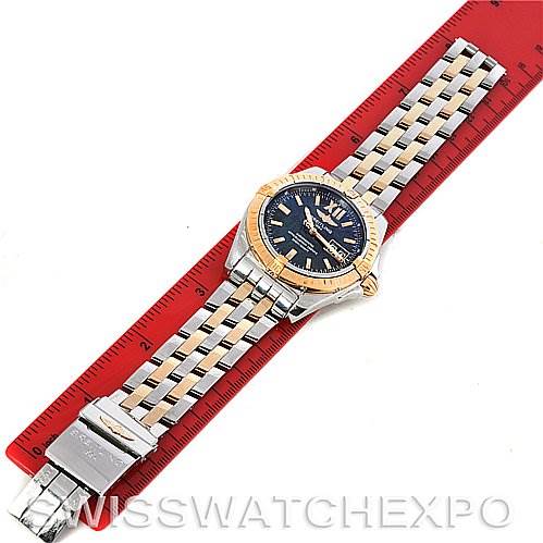 This image shows a Breitling Windrider C49350 Men's Steel and Gold (two tone) Black Dial C49350 Men's Steel and Gold (two tone) Black Dial watch laid flat on a red ruler, featuring a two-tone metal bracelet and a blue dial.