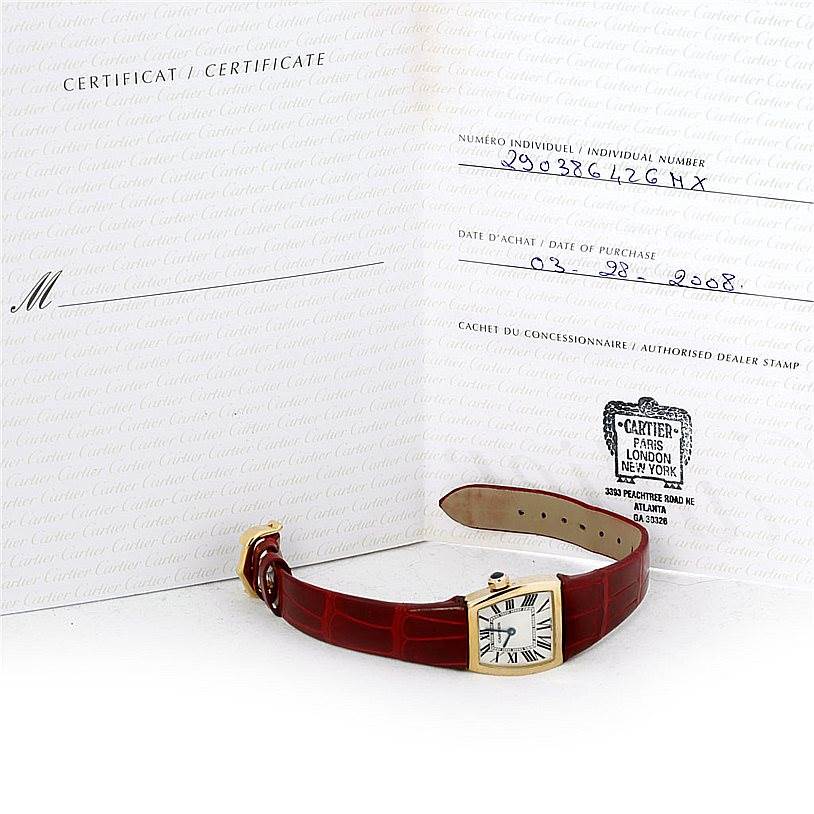 This image shows a Cartier La Dona W6400256 Women's Yellow Gold Silver Dial W6400256 Women's Yellow Gold Silver Dial watch with a red leather strap and its certificate, laid flat.