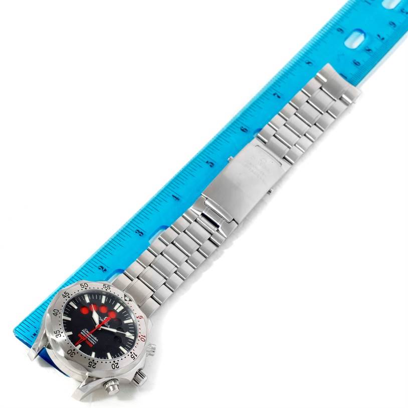 The Omega Seamaster 2595.50.00 Men
s Stainless Steel Black Dial 2595.50.00 Men
s Stainless Steel Black Dial watch is shown from a top-down angle, displaying its face, bezel, and metal bracelet placed alongside a blue ruler.