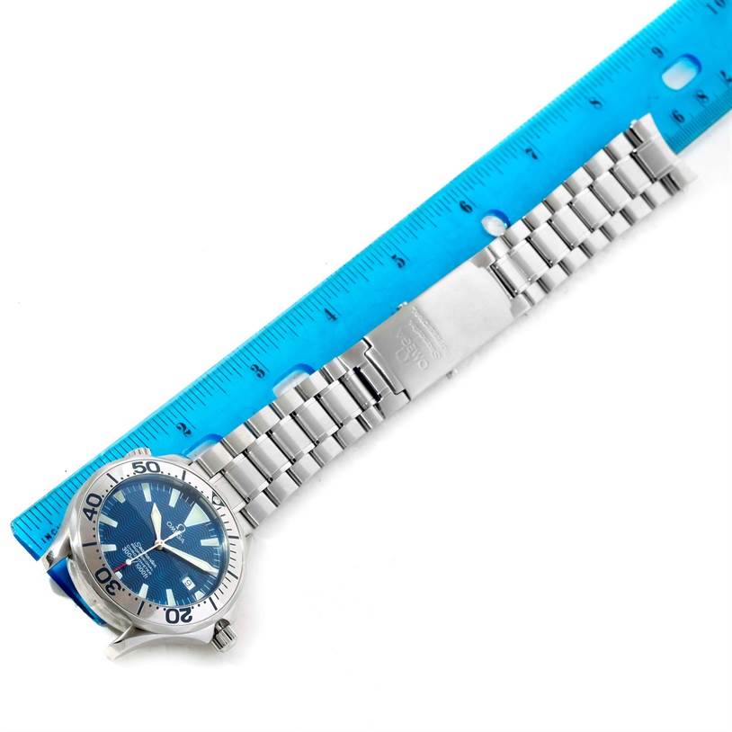 The image shows a top-down view of an Omega Seamaster 2255.80.00 Men
s Stainless Steel Blue Dial 2255.80.00 Men
s Stainless Steel Blue Dial watch with a stainless steel bracelet placed next to a blue ruler.