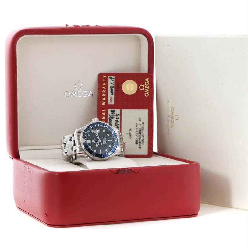 The image shows an Omega Seamaster 2561.80.00 Men
s Stainless Steel Blue Dial 2561.80.00 Men
s Stainless Steel Blue Dial watch in its red case, accompanied by a warranty card.