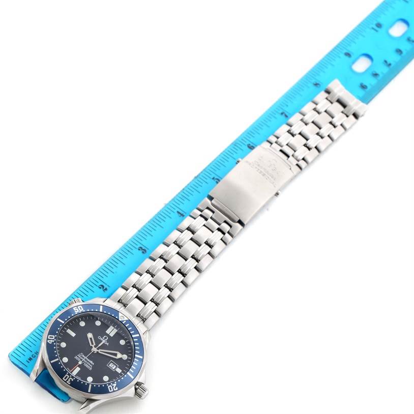 The Omega Seamaster 2541.80.00 Men
s Stainless Steel Blue Dial 2541.80.00 Men
s Stainless Steel Blue Dial watch is shown from a top-down angle with its face, bezel, and metal bracelet visible alongside a blue ruler.