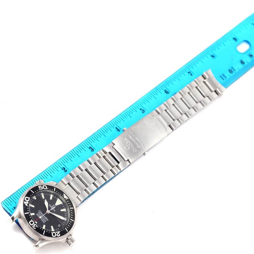 The image shows an Omega Seamaster 2252.50.00 Men
s Stainless Steel Black Dial 2252.50.00 Men
s Stainless Steel Black Dial watch with a metal bracelet positioned next to a blue ruler for scale.