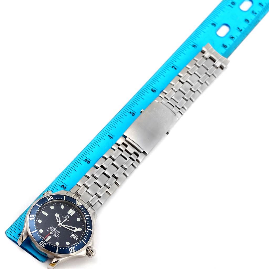 The image shows a side view of an Omega Seamaster 2531.80.00 Men
s Stainless Steel Blue Dial 2531.80.00 Men
s Stainless Steel Blue Dial watch with a blue dial and a stainless steel bracelet positioned alongside a blue ruler.