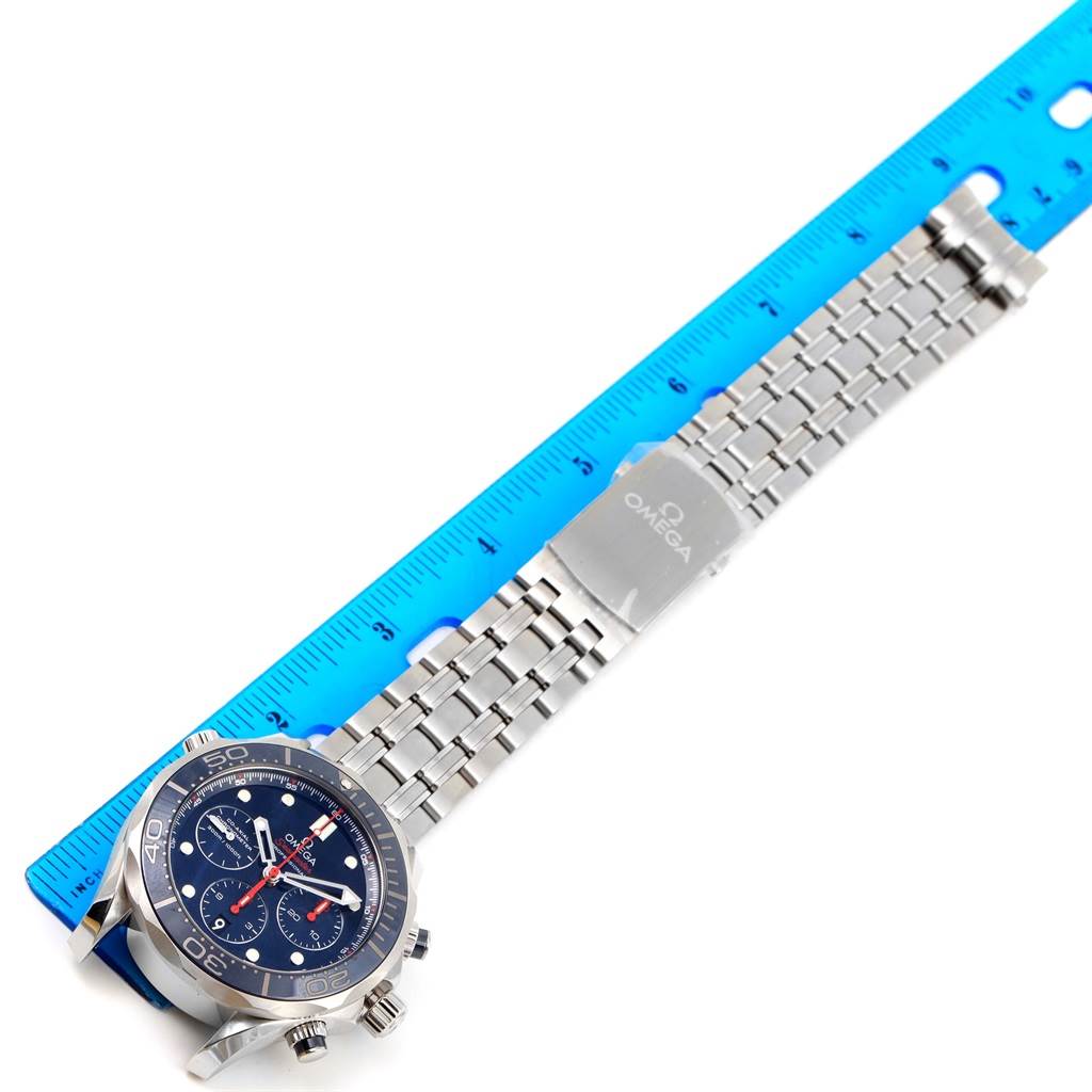 The image shows a top-down view of an Omega Seamaster 212.30.44.50.03.001 Men
s Stainless Steel Blue Dial 212.30.44.50.03.001 Men
s Stainless Steel Blue Dial watch and its metal band against a blue ruler.