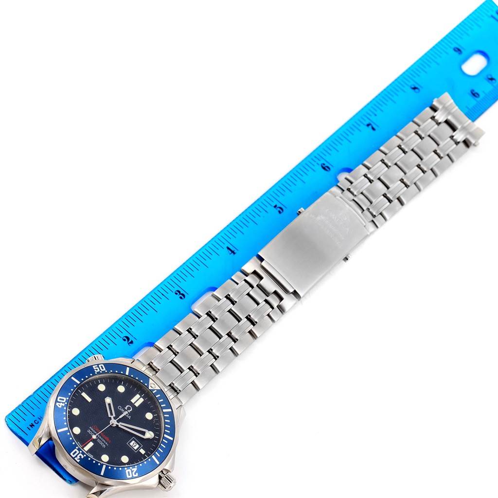 The Omega Seamaster 2221.80.00 Men
s Stainless Steel Blue Dial 2221.80.00 Men
s Stainless Steel Blue Dial watch is shown horizontally with its band extended alongside a blue ruler for measurement.