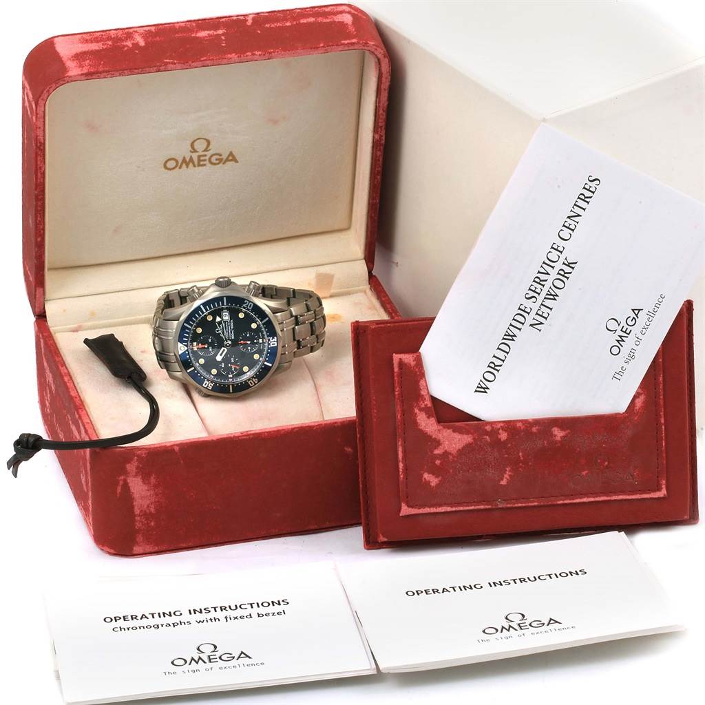 The Omega Seamaster 2298.80.00 Men
s Titanium Blue Dial 2298.80.00 Men
s Titanium Blue Dial watch is shown front-on in an open red velvet box, surrounded by instruction manuals and a service booklet.