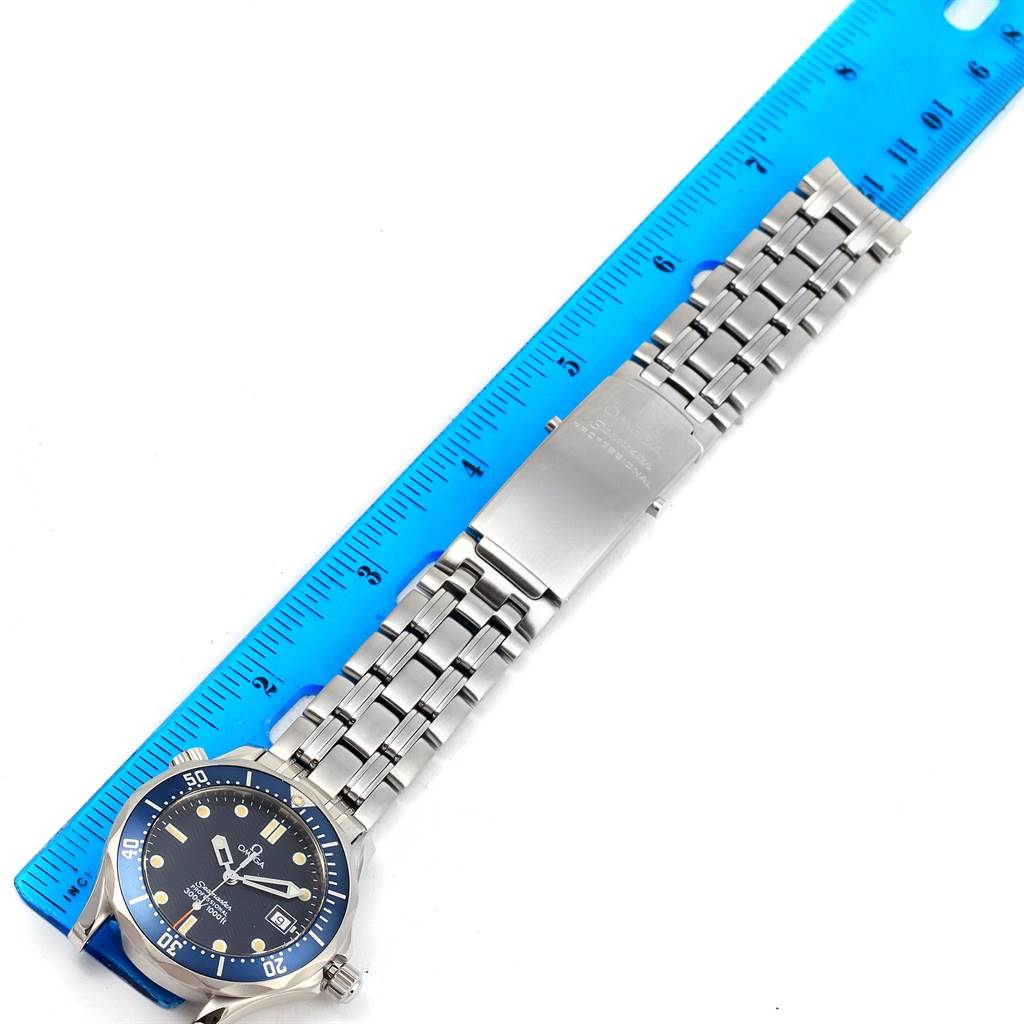 The image shows an overhead view of an Omega Seamaster 2561.80.00 Men
s Stainless Steel Blue Dial 2561.80.00 Men
s Stainless Steel Blue Dial watch with a stainless steel bracelet placed next to a blue ruler.