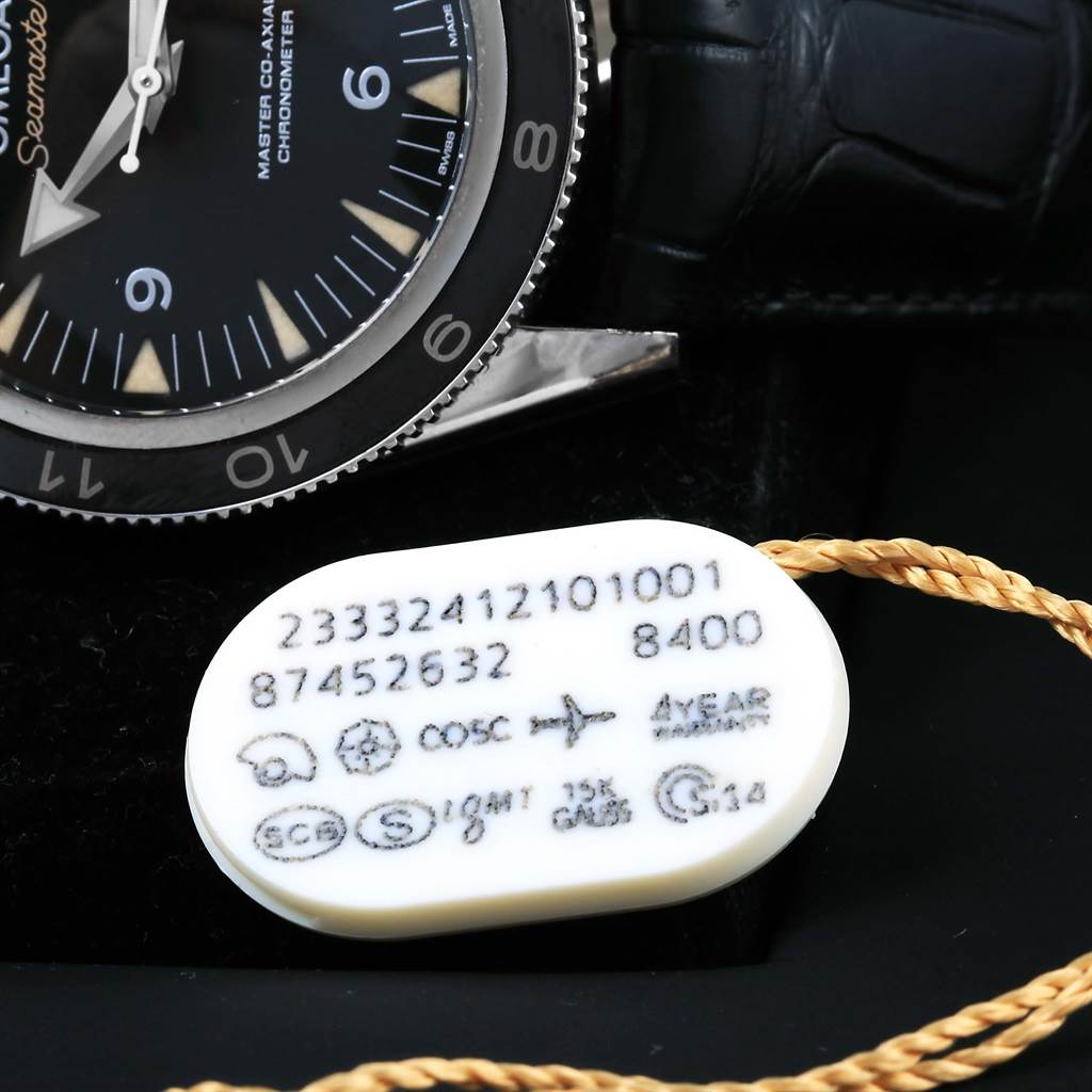 The image shows a partial view of an Omega Seamaster 233.32.41.21.01.001 Men's Stainless Steel Black Dial 233.32.41.21.01.001 Men's Stainless Steel Black Dial watch face, bezel, and a tag with serial numbers and certifications.