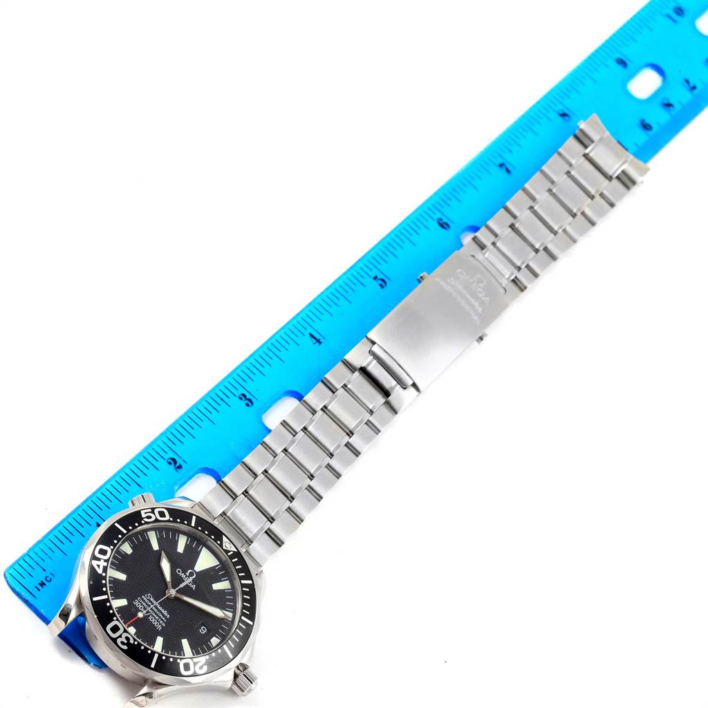 The Omega Seamaster 2254.50.00 Men
s Stainless Steel Black Dial 2254.50.00 Men
s Stainless Steel Black Dial watch is shown from an overhead angle, displaying the dial, bracelet, and clasp next to a blue ruler.