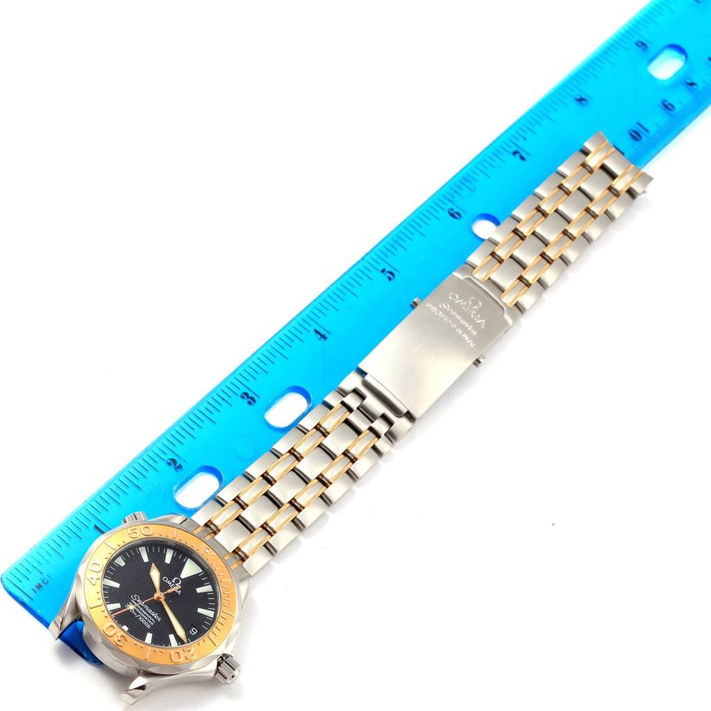 The image shows an Omega Seamaster Men
s Stainless Steel Black Dial Men
s Stainless Steel Black Dial watch laid flat next to a ruler, focusing on its bezel, dial, and metal bracelet.