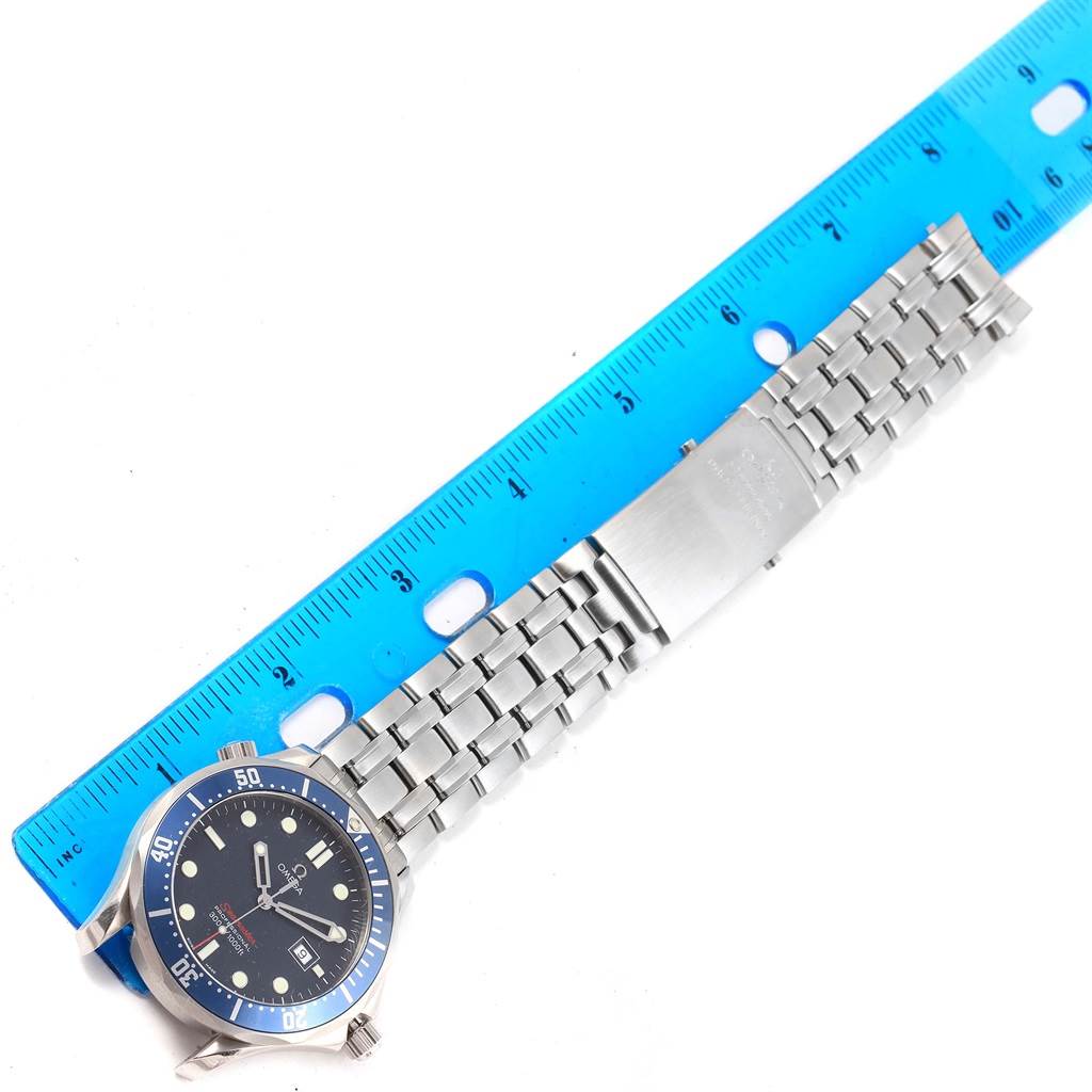 The image shows a side view of an Omega Seamaster 2221.80.00 Men
s Stainless Steel Blue Dial 2221.80.00 Men
s Stainless Steel Blue Dial watch placed next to a blue ruler.