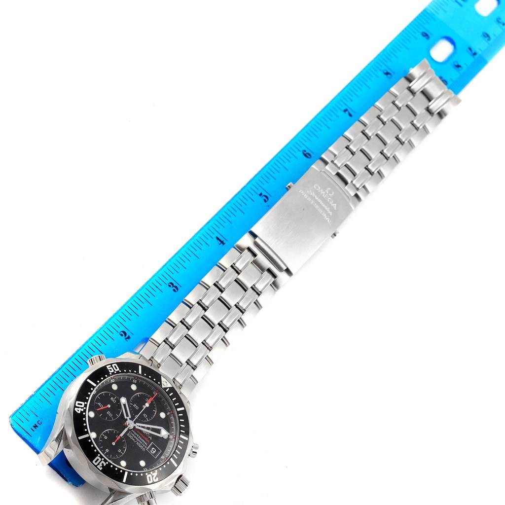 The Omega Seamaster 213.30.42.40.01.001 Men
s Stainless Steel Black Dial 213.30.42.40.01.001 Men
s Stainless Steel Black Dial watch is shown from a top-down angle, displaying its face, bezel, and metal bracelet laid next to a blue ruler.