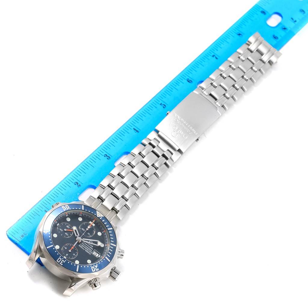 The image shows a top view of an Omega Seamaster 2599.80.00 Men
s Stainless Steel Blue Dial 2599.80.00 Men
s Stainless Steel Blue Dial watch with its face, bezel, and metal bracelet next to a blue ruler.