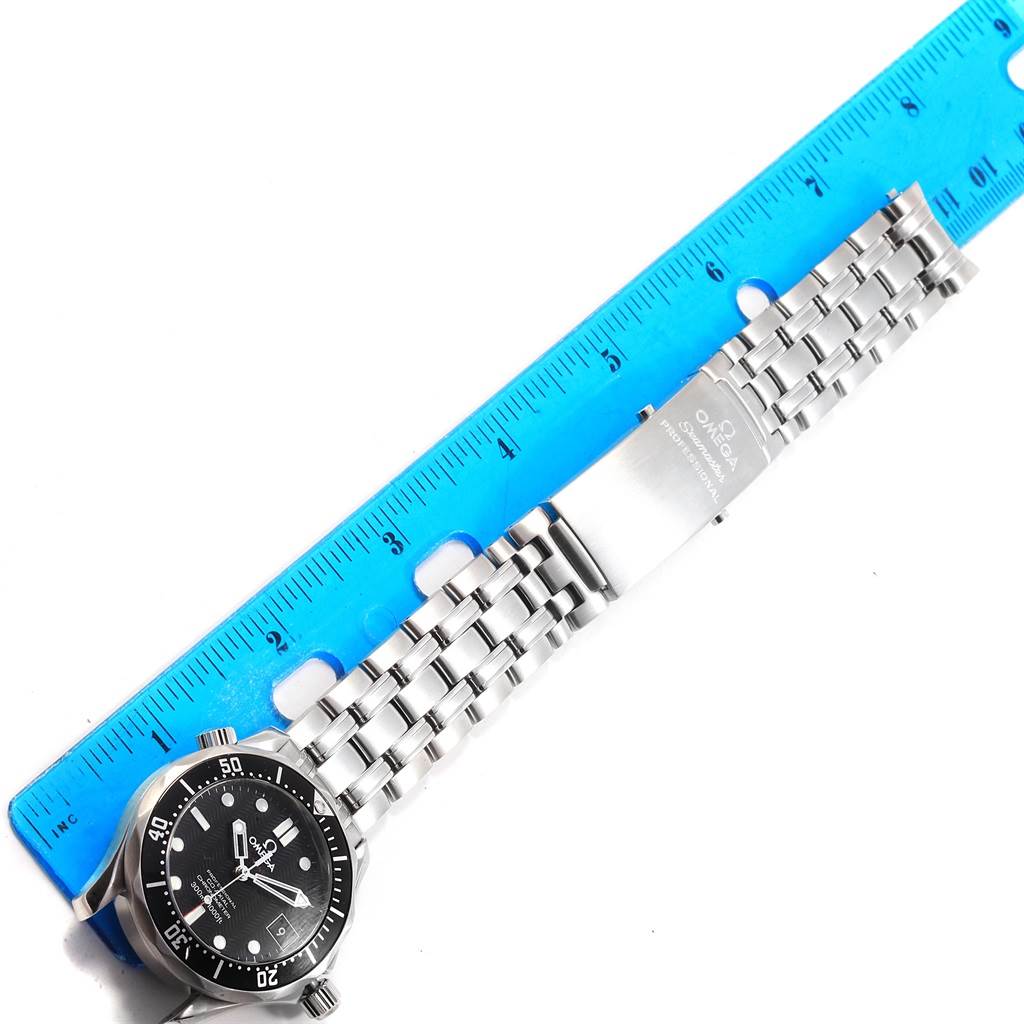 The image shows a top-down view of an Omega Seamaster 212.30.36.20.01.001 Men
s Stainless Steel Black Dial 212.30.36.20.01.001 Men
s Stainless Steel Black Dial watch with a stainless steel bracelet and clasp next to a blue ruler.