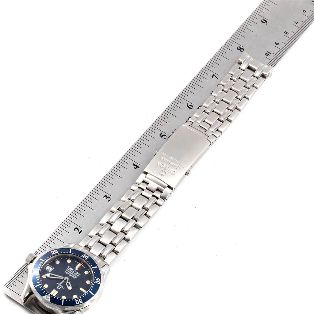 The Omega Seamaster 2551.80.00 Men
s Stainless Steel Blue Dial 2551.80.00 Men
s Stainless Steel Blue Dial watch is shown from a top-down angle, displaying its face, bezel, and metal bracelet on a ruler.