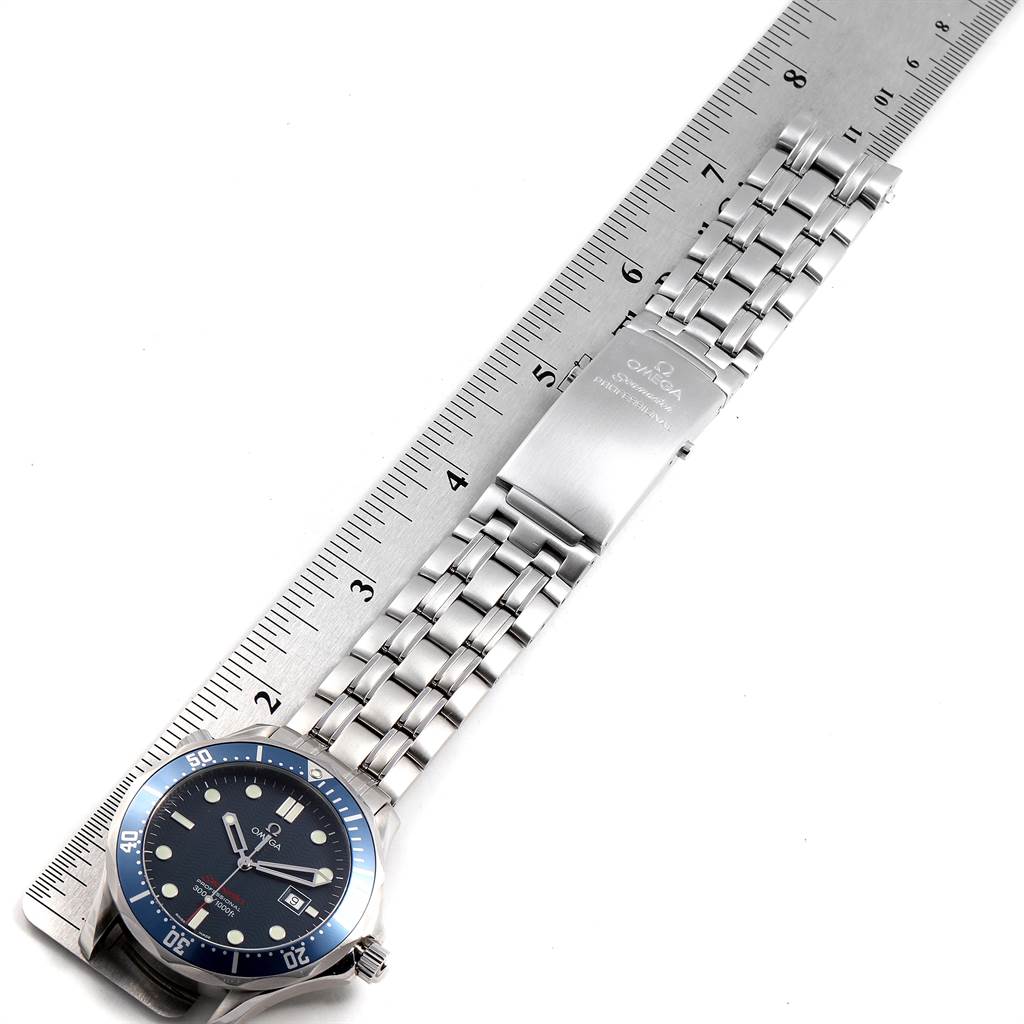 The Omega Seamaster 2221.80.00 Men
s Stainless Steel Blue Dial 2221.80.00 Men
s Stainless Steel Blue Dial watch is laid flat on a ruler, showing its face, bezel, and metal bracelet with clasp.