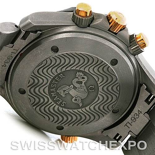 The image shows the back case and crown of an Omega Seamaster 2294.50.00 Men's Titanium Black Dial 2294.50.00 Men's Titanium Black Dial watch, highlighting its intricate wave pattern and gold crown accents.