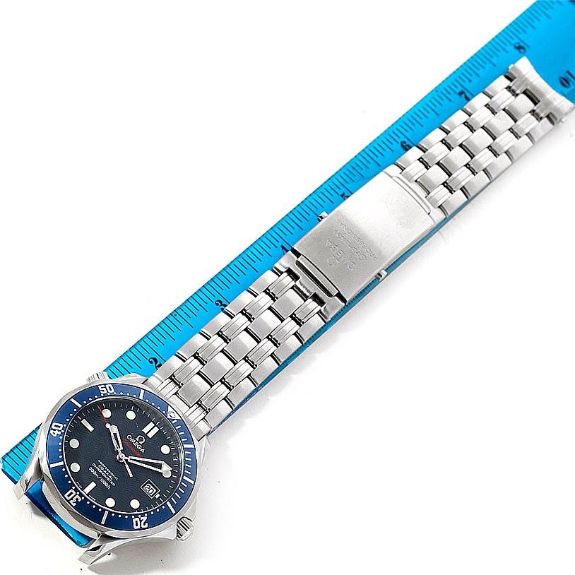 The Omega Seamaster 2220.80.00 Men
s Stainless Steel Blue Dial 2220.80.00 Men
s Stainless Steel Blue Dial watch is shown from a top-down angle, displaying its face, bezel, and metal bracelet laid next to a blue ruler.