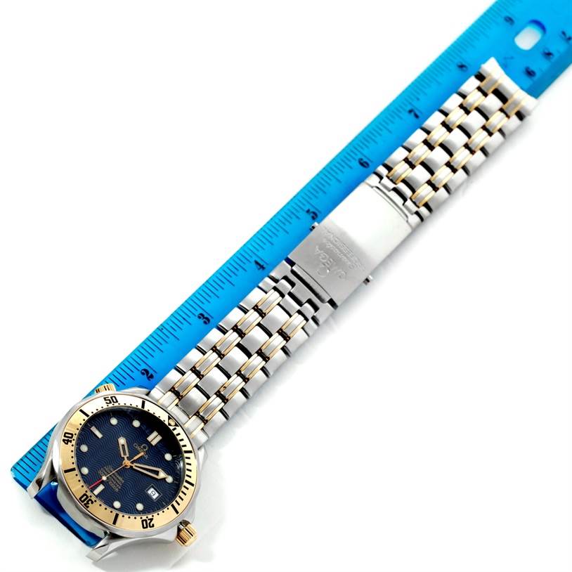 The image shows a top-down view of an Omega Seamaster 2332.80.00 Men
s Stainless Steel Blue Dial 2332.80.00 Men
s Stainless Steel Blue Dial watch, including its face, bezel, bracelet, and clasp next to a blue ruler.