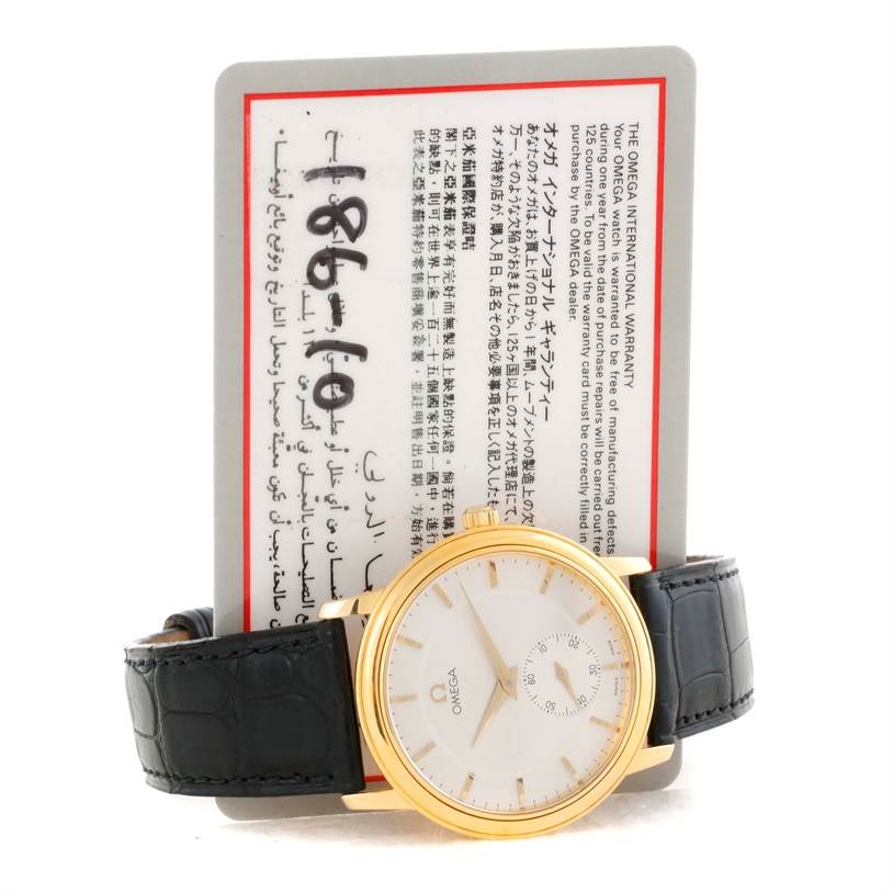 This image shows an Omega De Ville 4620.31 Men's Yellow Gold Silver Dial 4620.31 Men's Yellow Gold Silver Dial watch with a gold case and black leather strap, positioned in front of its warranty card.