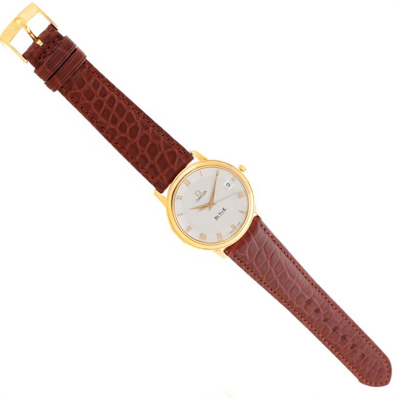 The Omega De Ville Men's Yellow Gold Silver Dial Men's Yellow Gold Silver Dial watch is shown from a top-down angle, displaying the entire strap, dial, and case.