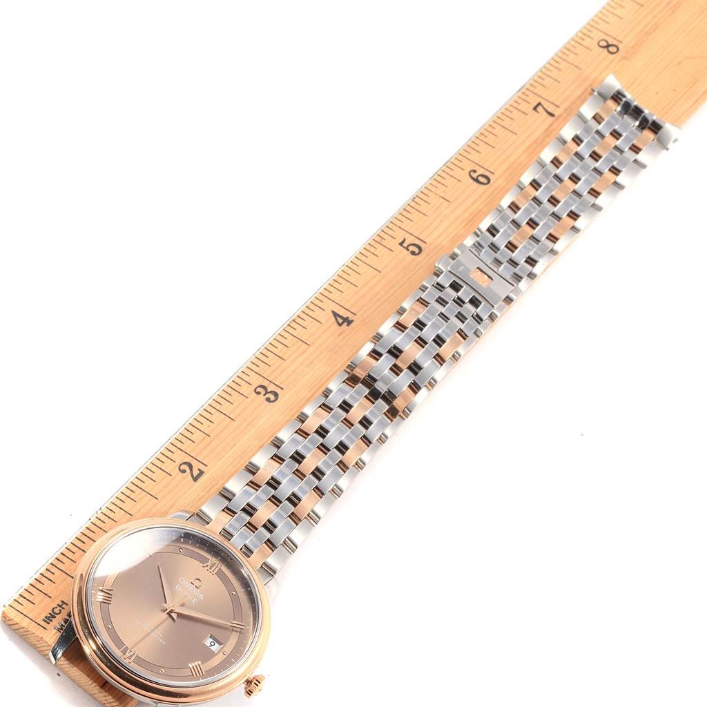 The image shows a De Ville model by Omega placed next to a ruler, illustrating the watch's full face, dial, and metal strap.