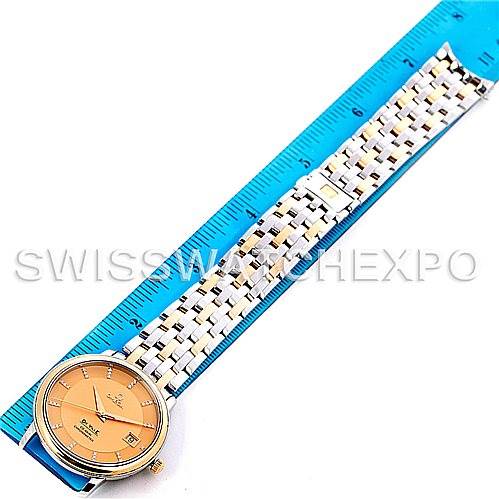 The image shows an overhead view of an Omega De Ville 4374.15.00 Men
s Steel and Gold (two tone) Champagne Dial 4374.15.00 Men
s Steel and Gold (two tone) Champagne Dial watch, displaying its face and metal bracelet alongside a blue ruler.