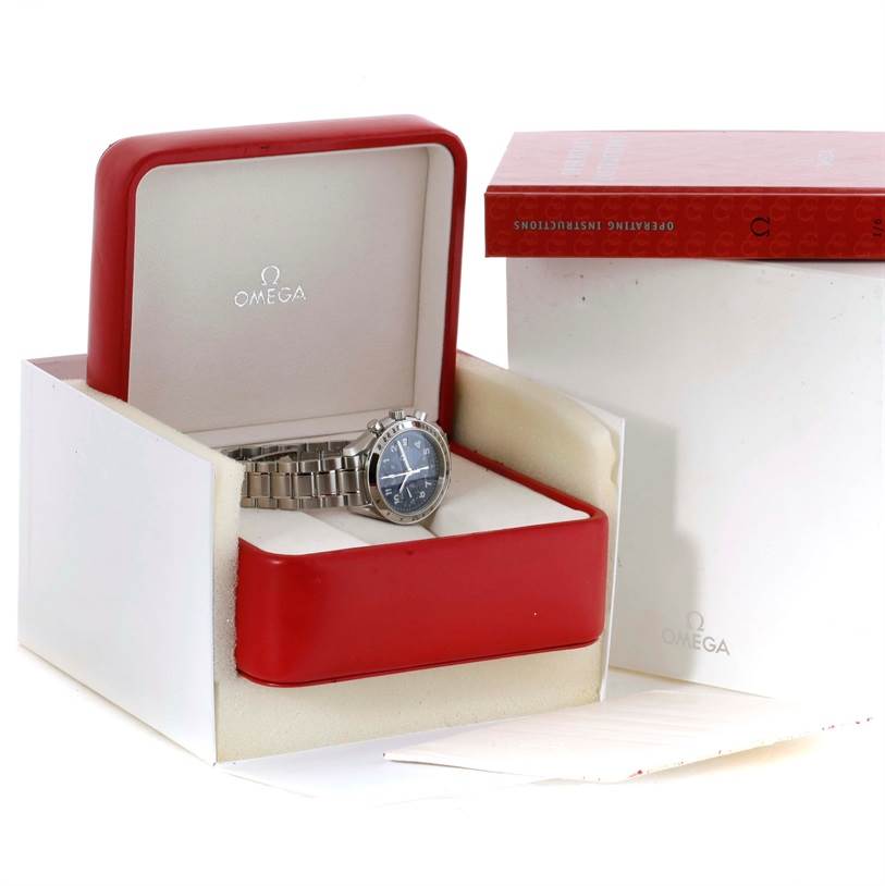 The Omega Speedmaster Men
s Stainless Steel Blue Dial Men
s Stainless Steel Blue Dial watch is shown at a slight angle inside an open red box, with instruction manuals next to it.