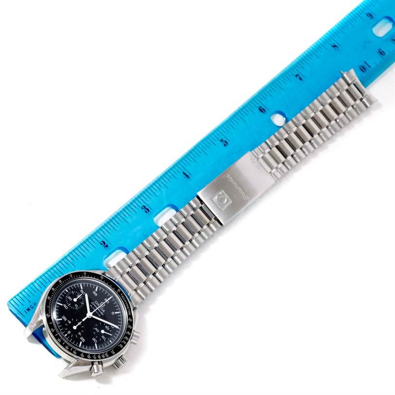 The image shows an Omega Speedmaster 3510.50.00 Men
s Stainless Steel Black Dial 3510.50.00 Men
s Stainless Steel Black Dial watch laid flat, displaying its face and metal band against a blue ruler for scale.