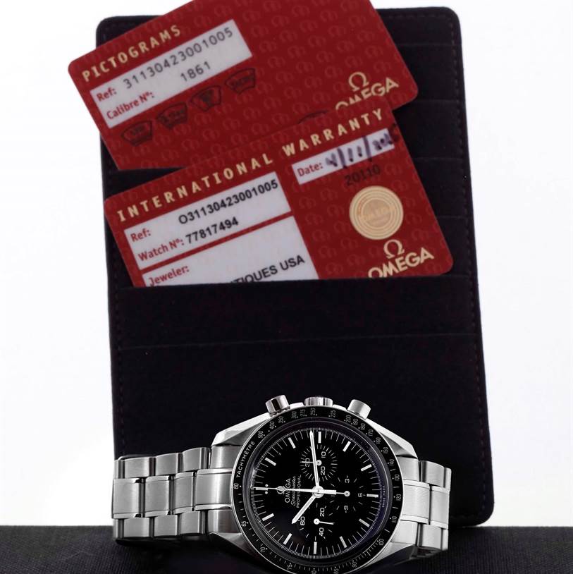 The image shows an Omega Speedmaster 311.30.42.30.01.005 Men
s Stainless Steel Black Dial 311.30.42.30.01.005 Men
s Stainless Steel Black Dial watch laid flat with its international warranty cards placed behind it.