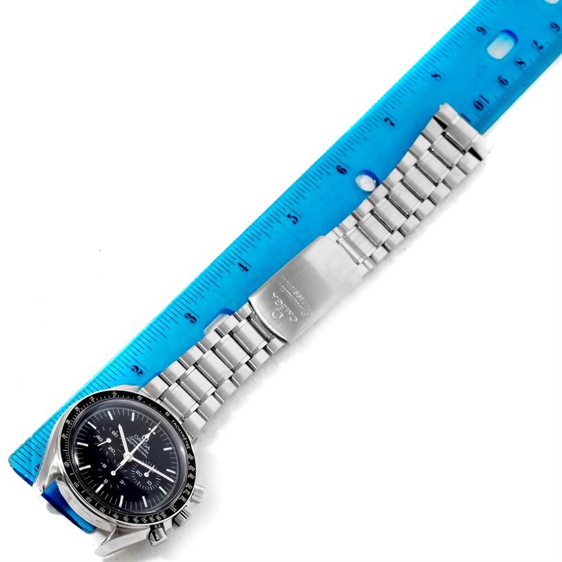 The image shows an Omega Speedmaster 3570.50.00 Men
s Stainless Steel Black Dial 3570.50.00 Men
s Stainless Steel Black Dial watch laid flat with a blue ruler for scale.