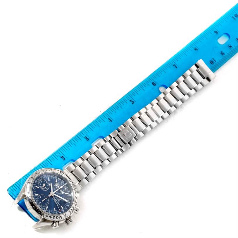 The image shows a top-down view of an Omega Speedmaster 3523.80.00 Men
s Stainless Steel Blue Dial 3523.80.00 Men
s Stainless Steel Blue Dial watch with a stainless steel bracelet next to a blue ruler.