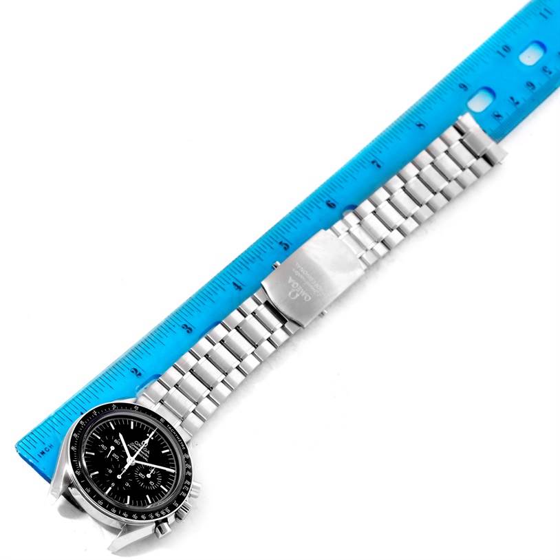 The Omega Speedmaster 3573.50.00 Men
s Stainless Steel Black Dial 3573.50.00 Men
s Stainless Steel Black Dial watch is shown at a top-down angle, with its face, bracelet, and clasp visible next to a blue ruler.