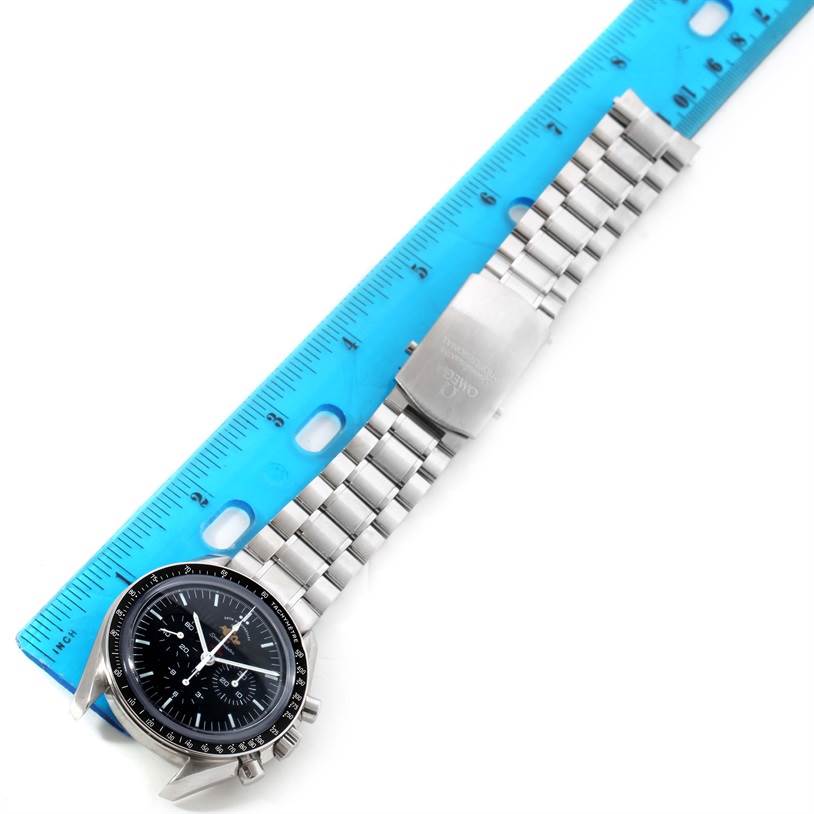 The Omega Speedmaster 311.30.42.30.01.001 Men's Stainless Steel Black Dial 311.30.42.30.01.001 Men's Stainless Steel Black Dial watch is shown from a top-down angle, including the face and metal bracelet next to a blue ruler.