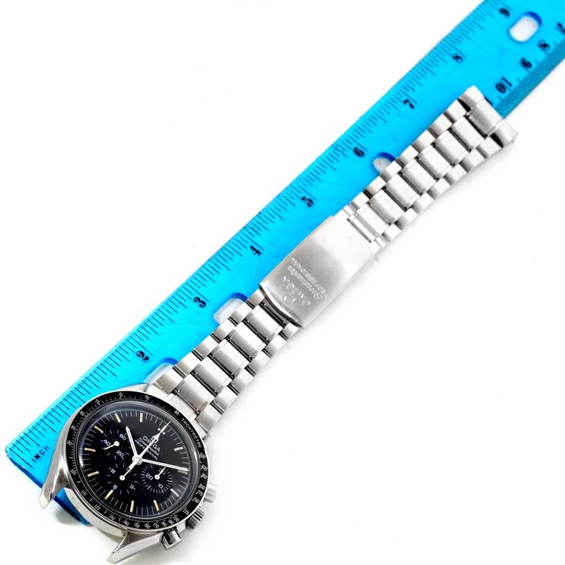 This image shows the Omega Speedmaster Men
s Stainless Steel Black Dial Men
s Stainless Steel Black Dial watch from an overhead angle, including its face and metal bracelet next to a blue ruler for scale.