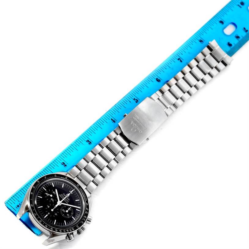 The Omega Speedmaster 3570.50.00 Men
s Stainless Steel Black Dial 3570.50.00 Men
s Stainless Steel Black Dial watch is shown from a top-down angle, alongside a blue ruler, displaying its face, bracelet, and clasp.