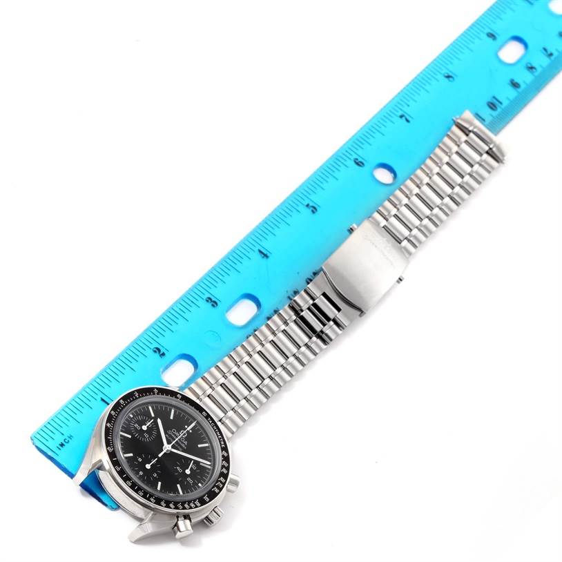 The image shows an Omega Speedmaster 3539.50.00 Men
s Stainless Steel Black Dial 3539.50.00 Men
s Stainless Steel Black Dial watch with its face and metal bracelet laid alongside a blue ruler.