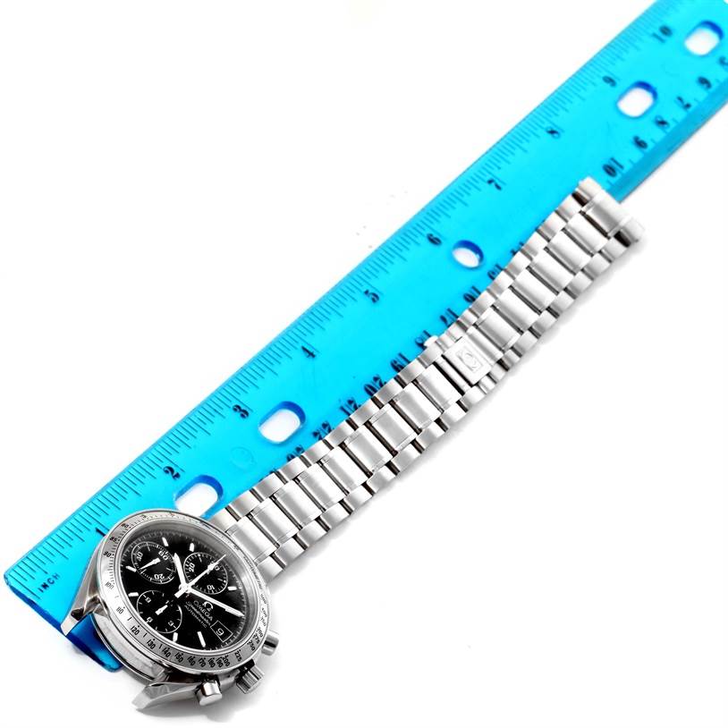 The Omega Speedmaster 3513.50.00 Men
s Stainless Steel Black Dial 3513.50.00 Men
s Stainless Steel Black Dial watch is shown from a top-down angle along with a metal bracelet and a blue ruler.
