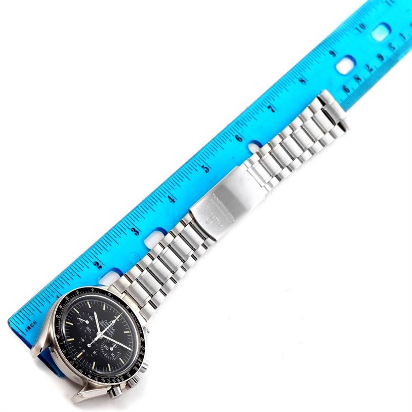 This image shows an Omega Speedmaster 3572.50.00 Men
s Stainless Steel Black Dial 3572.50.00 Men
s Stainless Steel Black Dial watch laid flat next to a ruler, fully displaying its face and metal bracelet.